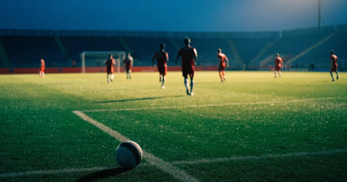 Ein Fußballstadion unter Flutlicht mit hellen Rängen, von einem Hügel aus gesehen, darüber ein dunkelblauer Abendhimmel.
