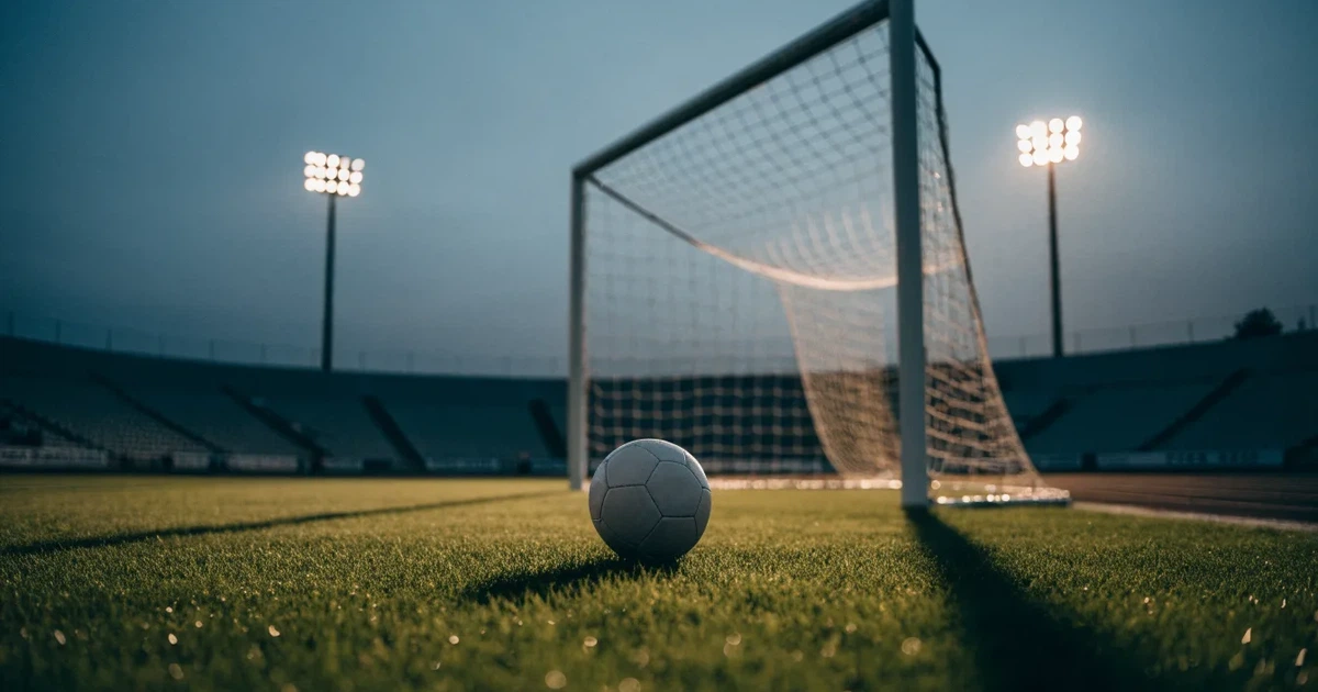 Ein Fußball liegt im Strafraum direkt vor dem Tor mit Netz, im Hintergrund leere Ränge bei Dämmerung.