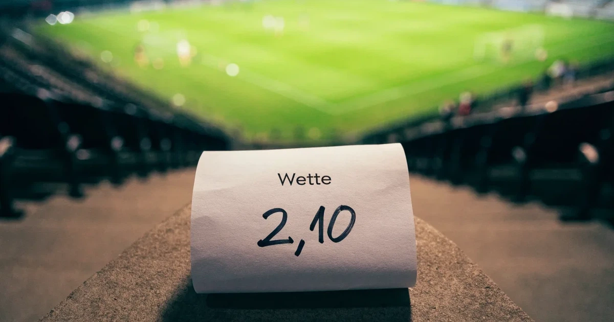 Leere Sitzreihen eines großen Stadions unter Flutlicht, dahinter die ferne Sicht auf den hell beleuchteten Rasen nach Sonnenuntergang.