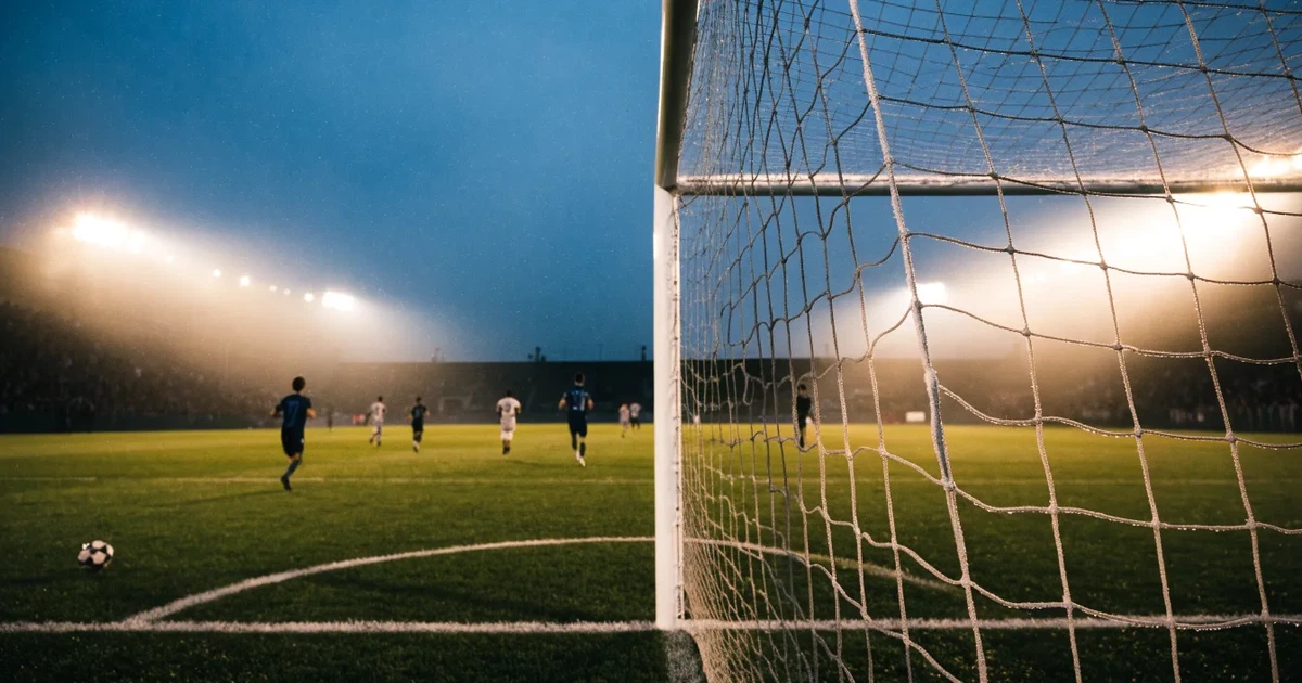 Ein Fußballtor mit Netz steht auf einem leeren Platz im Nebel der Morgendämmerung, der Rasen ist taufeucht.