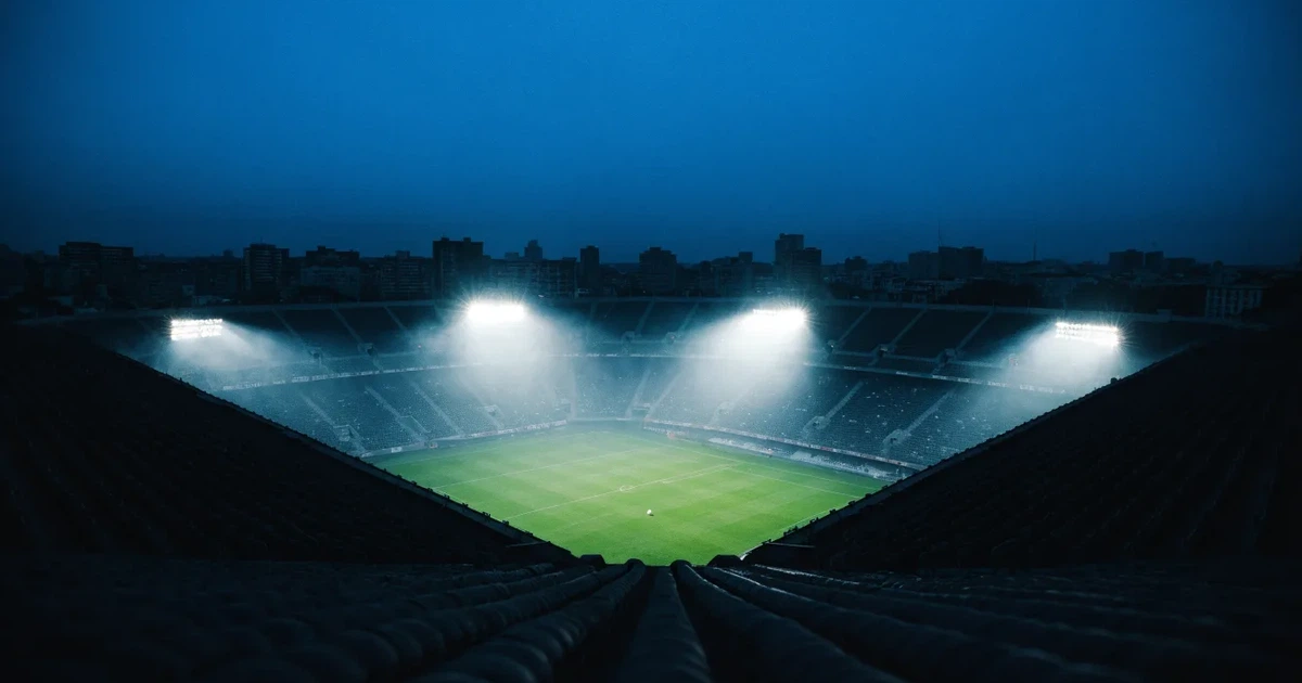 Ein Stadion bei Nacht unter Flutlicht aus der Ferne gesehen, der Rasen ist hell erleuchtet, keine erkennbaren Personen.