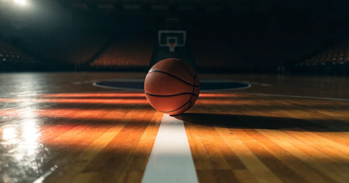 Ein Basketball liegt auf dem Parkettboden einer leeren Arena, Scheinwerfer werfen Licht auf die Mittellinie.