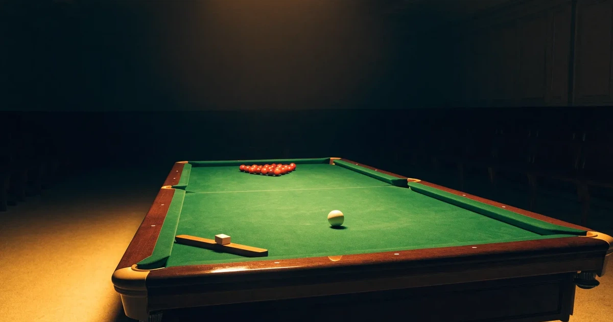 Ein Snookertisch mit grünem Tuch und aufgebauten roten Kugeln in einem abgedunkelten Raum unter einer hängenden Lampe.