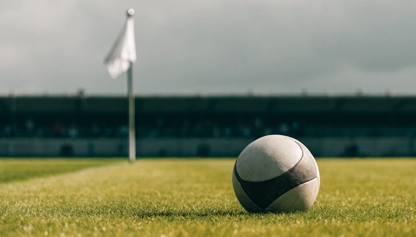 Ein Fußball liegt neben einer Eckfahne auf kurz gemähtem Rasen unter bewölktem Himmel.
